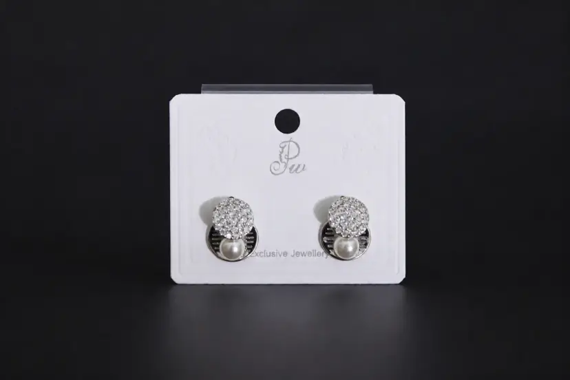 Pair of silver-toned geometric stud earrings featuring a round crystal pave disc and a small white pearl drop on a display card.