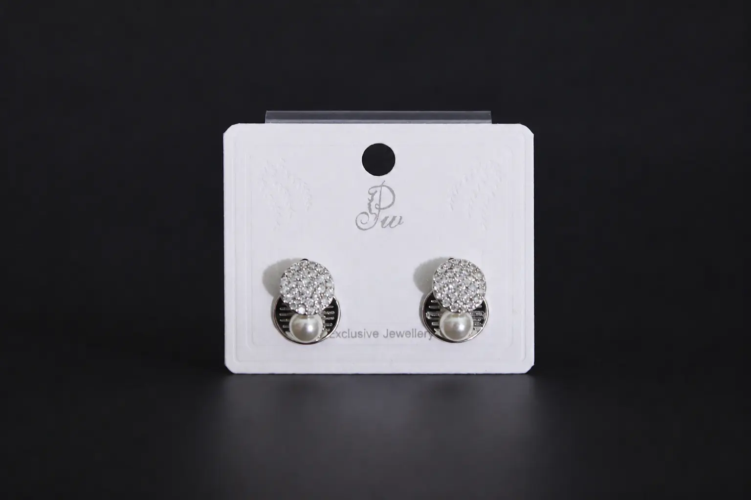 Pair of silver-toned geometric stud earrings featuring a round crystal pave disc and a small white pearl drop on a display card.